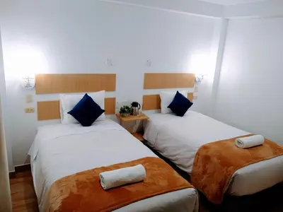 two beds in a room with white sheets and blue pillows at Emmanuel inn Machupicchu in Machu Picchu