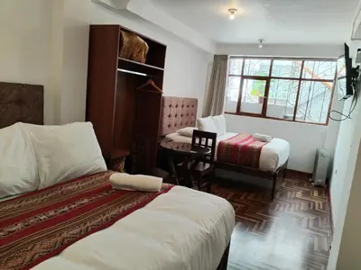 a room with two beds and a desk and a table at Paqarina San Blas in Cusco