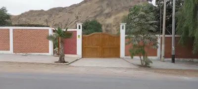 a brown wooden gate with a brick wall and a mountain at Las buganvilias in Pachacamac