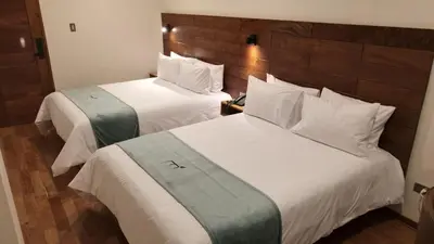 two beds in a hotel room with white sheets at Muña Hotel Andahuaylas in Andahuaylas