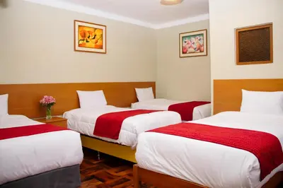 a room with three beds with red and white sheets at HOSTAL CASA INKAS in Cusco