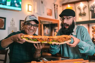 two men holding a large sandwich in a restaurant at Magar Hostel Bar in Cusco