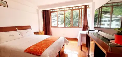 a bedroom with a bed and a desk and windows at Hotel Romero Machupicchu in Machu Picchu