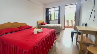 a bedroom with a bed with a red blanket and a table at Hospedaje Oxa Paraíso in Oxapampa