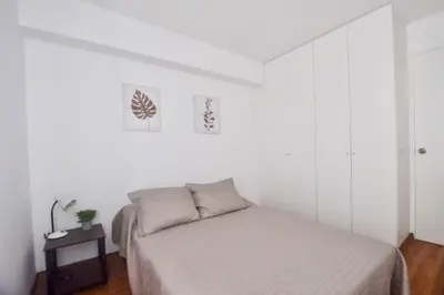 a white bedroom with a bed and a table at Hermoso y amplio departamento en zona tranquila en Jesús Maria in Lima