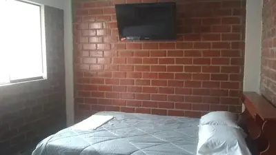 a bedroom with a brick wall with a bed and a flat screen tv at El Valle - Lunahuaná in Lunahuaná