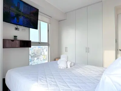a white bedroom with a large white bed with a flat screen tv at Peruvian Apartments Barranco 2004 in Lima