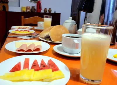 a table with plates of fruit and a glass of orange juice at Munay Ñusta Cusco in Cusco