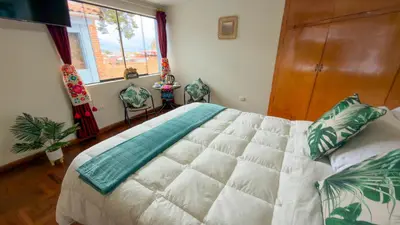 a bedroom with a bed with two chairs and a window at Apart Hotel de Alegria in Cusco