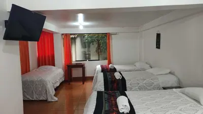 a room with three beds and a flat screen tv at Tierra Mágica Hostal in Machu Picchu