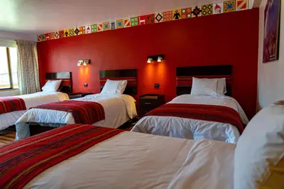 a room with three beds with red walls at Hotel Tierra Inka Sacred Valley in Ollantaytambo
