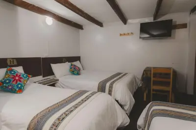 a room with two beds and a television on the wall at Lucios Cusco in Cusco