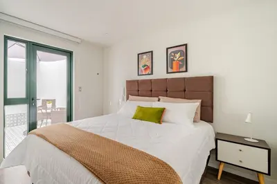 a white bedroom with a large bed with a green pillow at Vacation Escape - Elegant Barranco Stay near Beach & Art in Lima