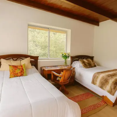a bedroom with two beds and a table and a window at La Casita de Orfi in Calca