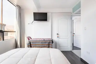 a white bedroom with a bed and a tv on the wall at Casa Monacó in Cusco