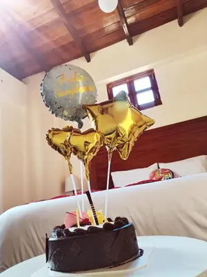 a chocolate cake on a table with balloons on a bed at NUNA SUMAQ Hotel in Ollantaytambo