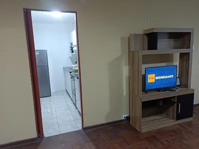 a room with a television on a stand and a kitchen at Alojamientos Perú II in Lima