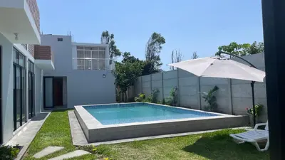 a swimming pool with an umbrella next to a house at Casa de Campo Aucallama in Huaral