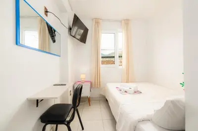 a small white bedroom with a bed and a desk at Retablo Boutique Hotel in Ayacucho
