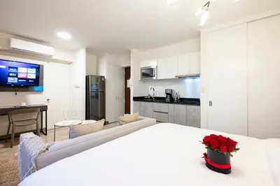 a room with a white bed and a kitchen at Connect Studios by Vibrant in Lima