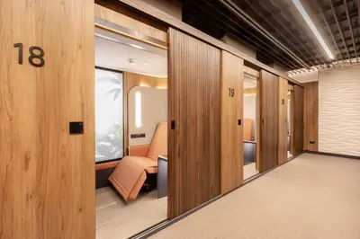 a hallway with wooden doors and a room with a chair at Sleepover - Lima Airport, the only in-terminal sleep pods in Lima