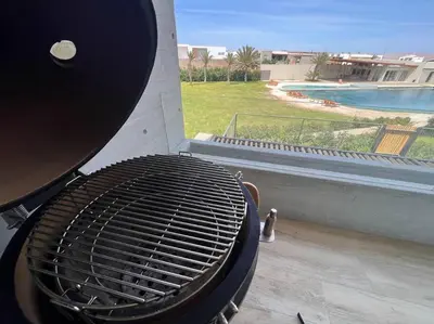 a grill on a patio with a view of a pool at Aldea 2BR TVs, KamadoBBQ for 6, Gym,Pool and Cowork in Paracas