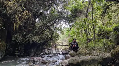 a person sitting on a rock by a stream at EcoLodge Mayu Camping in Tanca