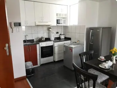 a kitchen with white appliances and a table with chairs at Edificio La Católica in Lima