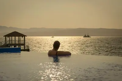 a woman sitting in a infinity pool looking at the ocean at Apartamento Frente a Islas Ballestas in Paracas