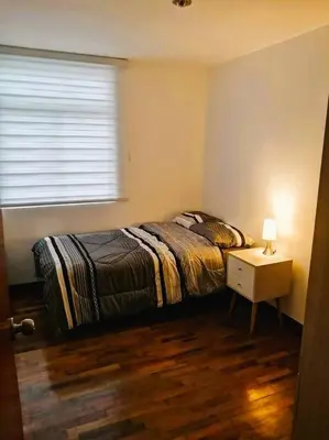 a bedroom with a bed and a nightstand and a window at Departamento con Cochera in Lima