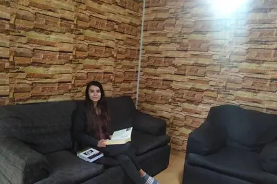 a woman sitting on a couch with a book at Apartamento 3Hab Seguridad y Cerca del Aeropuerto in Lima