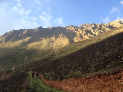 two people walking down a dirt path in front of a mountain at SAMAY WASI Rest house in Ollantaytambo