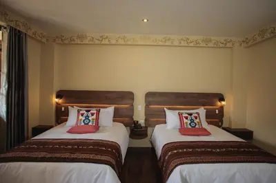 two beds in a hotel room with white sheets and red pillows at Valle Del Sol in Urubamba