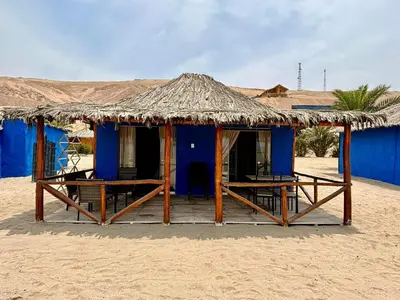 a blue hut with a straw roof on the beach at Bungalows frente al mar en playa Wakama in San Vicente de Cañete