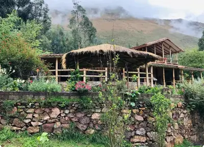 a house with a thatch roof and a stone wall at SAMAY WASI Rest house in Ollantaytambo