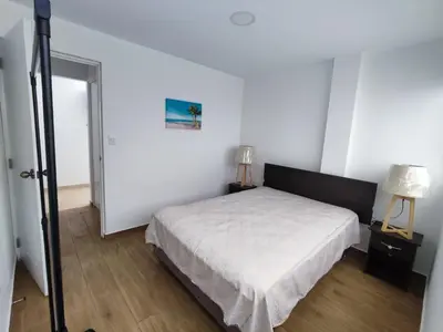 a white bedroom with a bed and a lamp at Departamento de playa in Lima
