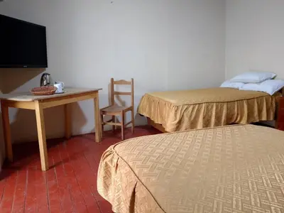 a room with two beds and a table and a chair at Frente al Qorikancha - 2 cuadras Plaza Central in Cusco