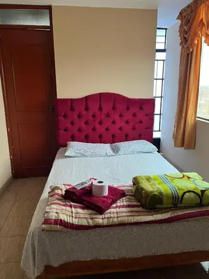 a bed with a red headboard with a cup on it at Hospedaje Monumental in Chincha
