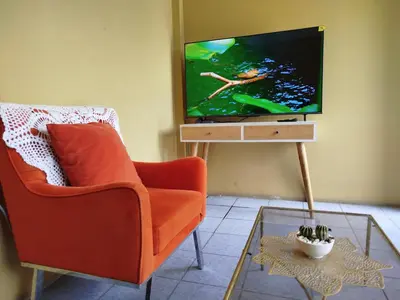 a living room with an orange chair and a flat screen tv at Apart Hotel Valdelomar in Ayacucho