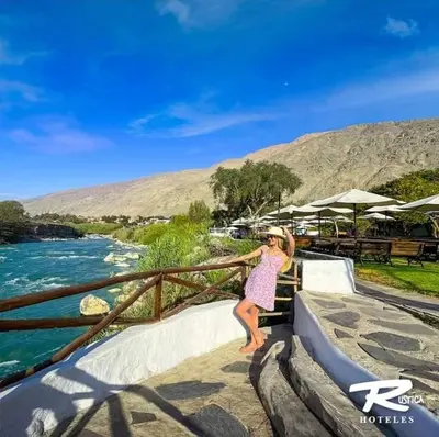 a woman in a pink dress leaning on a fence next to a river at Hotel Rustica Lunahuana in Uchupampa
