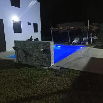 a person sitting on a bench next to a swimming pool at night at Chinchacampoymar Casa de playa en Chincha in Chincha Baja