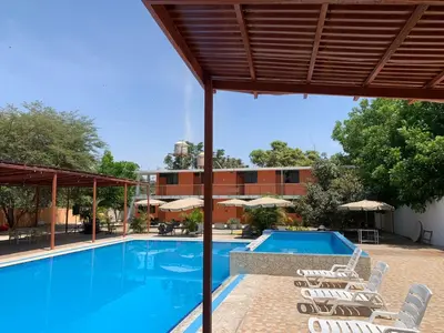 a swimming pool with chairs and a building at Hotel Los Pecanos in Ica