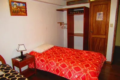 a bedroom with a red bed and a table with a lamp at Hospedaje Kamila in Cusco