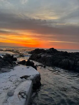 a sunset over the ocean with rocks in the water at Tanaka Beach House in Tanaca