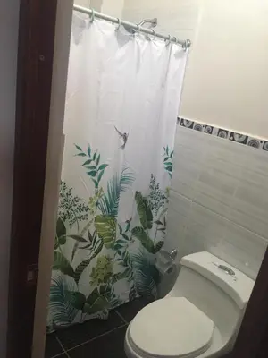 a bathroom with a toilet and a shower curtain with plants at Casa Hospedaje Las Lomas con piscina en La Merced in La Merced