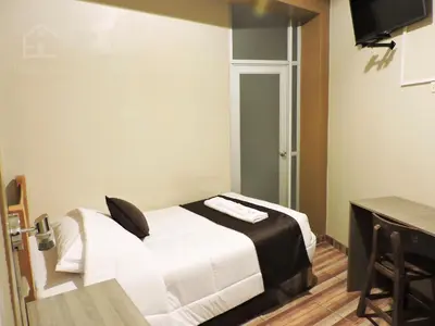 a bedroom with a bed with white sheets and a television at EmbajadaWanka in Huancayo