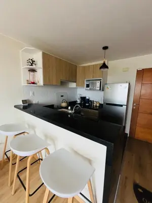 a kitchen with white chairs and a black counter top at Apartamento moderno en San Miguel in Lima