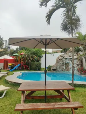 a picnic table with an umbrella in front of a pool at Tambo II Hotel Campestre in Cieneguilla