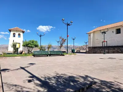 a park with two green benches and a white building at Jerusalen Inn -Dep 1 in Cusco