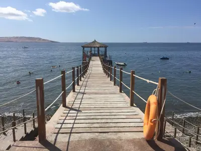 a wooden pier with an orange boat on the water at Paracas Beach Vacation Rentals in Paracas
